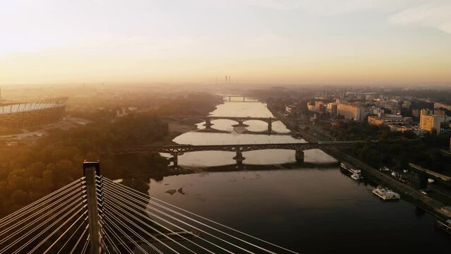 Aerial drone shot of PGE Narodowy national stadium and Swietokrzyski bridge in Warsaw city backlit with warm sunrise sun light, beautiful misty autumn morning, sunny dusk dawn orange colour, cityscape