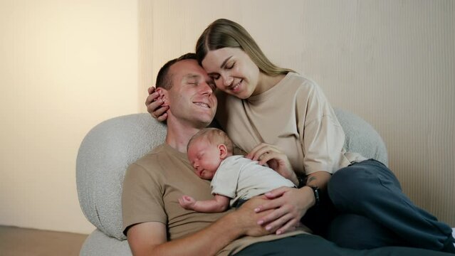 Relaxed Caucasian people having good time together. Couple sit on sofa with their newborn sleeping on dad's chest.