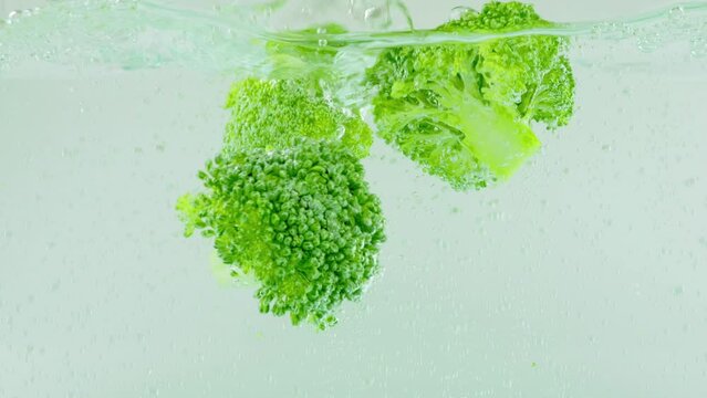 Green broccoli florets fall into boiling water with air bubbles.