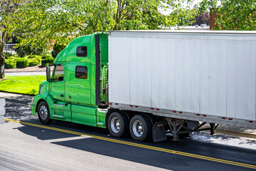 High cab big rig green semi truck transporting cargo in dry van semi trailer running on the city...
