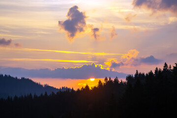 Colorful clouds in the sky at sunset against the backdrop of a mountainous forest area.