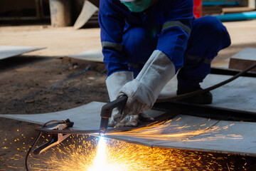 Worker cutting steel plate with Plasma Cutting process. Plasma cutting is a process that cuts through electrically conductive materials by means of an accelerated jet of hot plasma. - obrazy, fototapety, plakaty