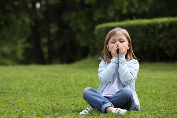 Fototapeta premium Little girl suffering from seasonal spring allergy on green grass in park. Space for text