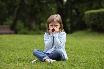 Fototapeta premium Little girl suffering from seasonal spring allergy on green grass in park