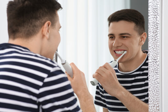 Man brushing his teeth with electric toothbrush near mirror in bathroom