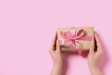 Woman holding gift box with bow on pink background, top view. Space for text