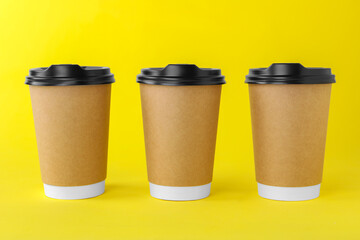 Paper cups with black lids on yellow background. Coffee to go