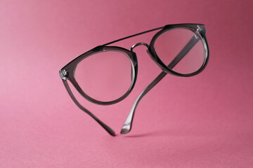 Stylish pair of glasses with plastic frame on pink background