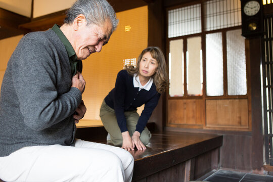 玄関で胸を押さえるシニア男性と様子を伺うシニア女性