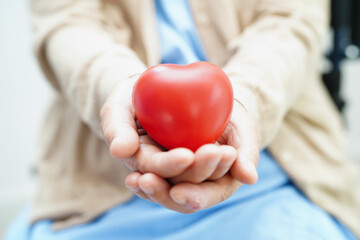 Asian elder senior woman patient holding red heart in hospital.