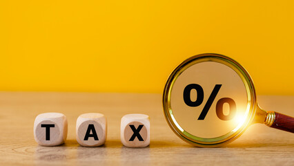 Tax concept with wooden cubes and magnifying glass on a yellow background. Tax payment reminder or annual taxation concept.