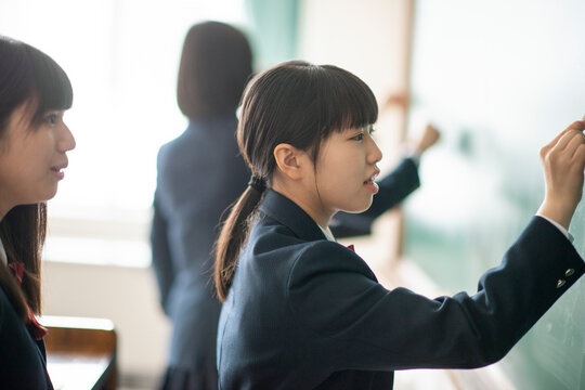 チョークで黒板に答えを書く女子学生