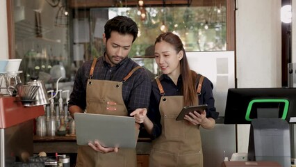 Cafe small business coffee shop owner couple wearing apron receive online orders from tablet or notebook, Indian husband man and Asian wife business partner check follower  from social media promotion