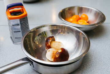 a set of kitchen utensils before cooking, stainless steel bowls, a grater and defrosted porcini mushrooms, a metal frying pan on a kitchen table.