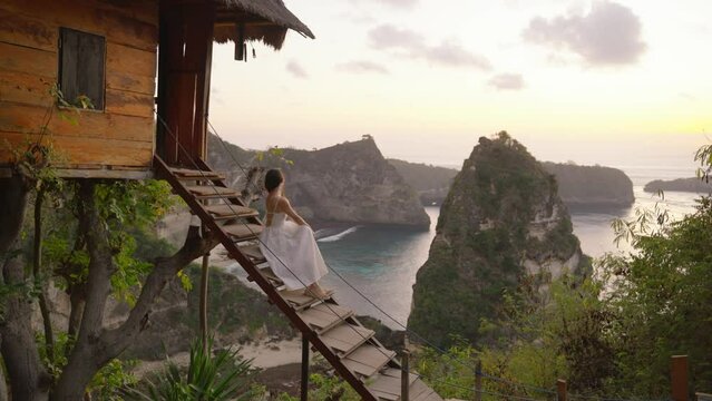 Nusa penida, Bali, indonesia, 4K video of woman white dress sit of tree house and looking at Atuh beach on tree house, Nusa Penida island at sunrise. Popular travel destination on Bali, indonesia.