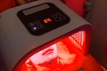 A female patient undergoes red LED light or RLT therapy for skin rejuvenation at an aesthetic clinic. Using a phototherapy device with red light wavelength for acne treatments and collagen production. - obrazy, fototapety, plakaty