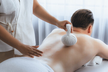 Hot herbal ball spa massage body treatment, masseur gently compresses herb bag on man body....