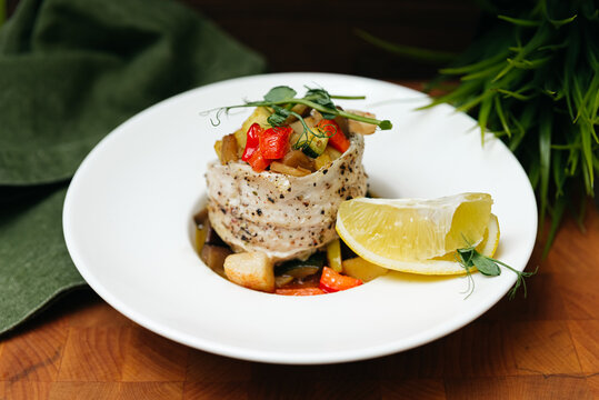 Sea bass fillet baked in cider with pieces of apples, red sweet pepper and zucchini. Serve with a slice of lemon and garnish with pea microgreens. Fish fillet with vegetables.