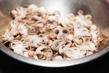 Raw fresh octopus in a stainless steel bowl on black background. Small octopuses before cooking.