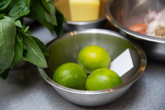 Ingredients for making sauce - lime, basil and butter. a metal bowl filled with limes on top of a counter.