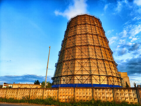 CHP cooling towers from which smoke is coming out against blue sky. A large pipe of a thermal power plant with smoke and steam on a blue sky background
