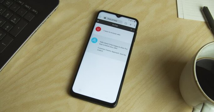 Artificial Intelligence - AI chat bot app on smartphone - Royalty free phone and app interface - Medium shot, work desk, laptop - "5 ways to increase sales"