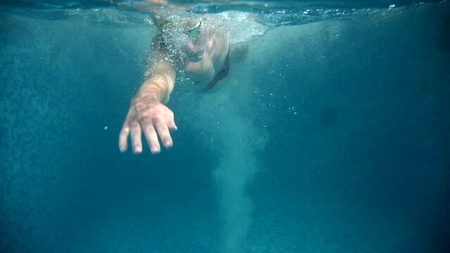 Underwater view of professional swimmer training in swimming pool, 4k 120 fps super slow motion raw video. Triathlete swim in black wetsuit 