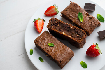 Chocolate brownie cut into portions and decorated with strawberries and mint.