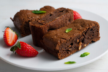 Fototapeta na wymiar Chocolate brownie cut into portions and decorated with strawberries and mint.