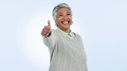 Face, smile and senior woman with thumbs up, agreement and promotion on blue studio background. Portrait, mature person or happy model with hand gesture, icon and feedback with review, emoji and like