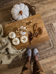 Cozy autumn house interior. Women's feet in felt slippers and corduroy trousers next to an oak bench with autumn decor