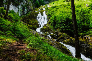 high white waterfall with rushing water in green hills during hiking in austria