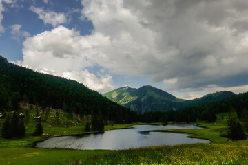 mountain lake with lot of green meadow and clouds with rain on blue sky