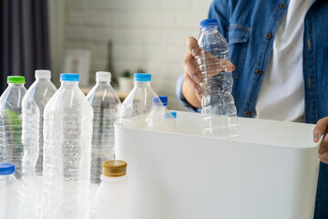 Asian woman separating trash for further recycling at home. She put plastic bottles into recycle box