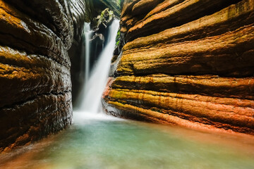 waterfall in the red canyon with layers of red rocks in a forest in austria