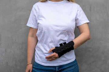 Faceless woman in white t-shirt with bandage on her hand for carpal tunnel syndrome on the grey background 