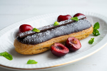 French eclairs filled with chocolate cream and served with fresh cherries.