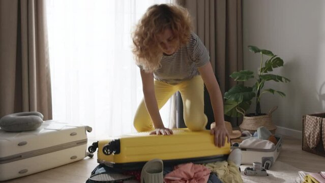 Spontaneous woman throwing clothes into suitcase without order organization to quickly pack up before traveling tourism journey. Traveler trying to pack things close suitcase with clothes sticking out