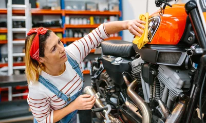 Foto auf Acrylglas Motorrad Concentrated mechanic woman cleaning fuel tank of custom motorcycle with a microfiber cloth and polish after repair on factory