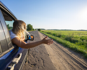 A woman catches the wind with her hand leaning out the car window. A beautiful woman enjoys a trip...
