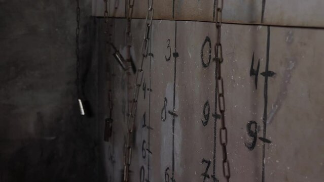  Close-up of chains hanging near a gray wall with various numbers and dashes in a dark scary room.