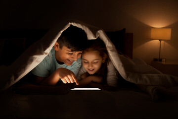 Brother and sister sharing digital tablet under sheet