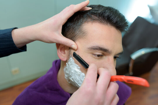 portrait of barber shaving mans chin