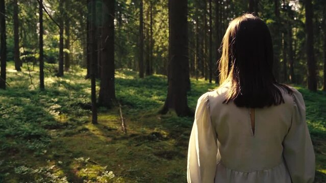 Camera approaches a young woman and takes her perspective which opens the view of the forest