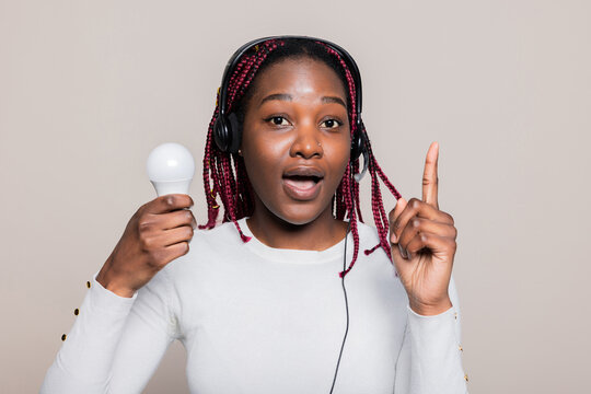 Delighted Smiley Attractive African American Woman With Braids Looking At Camera Have Interesting Idea Holding The Sign Lightbulb.