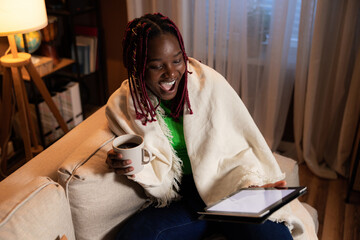 Beautiful young afro american woman with colourful braids smiling reading book online on tablet spending time