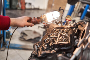 A car mechanic inspects the engine with a flashlight. Engine Block on a repair stand with Special crane jack. Technical service station for car.