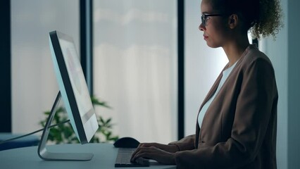 Black woman using desktop PC in dark office.