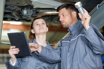 female and male mechanics standing underneath a car
