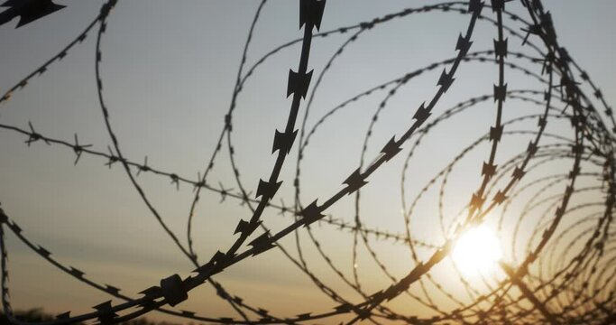 High barbed wire protect secret facility or military base, boundary barrier control prison isolated zone at sunset close up. Separation border line and barbwire for secure